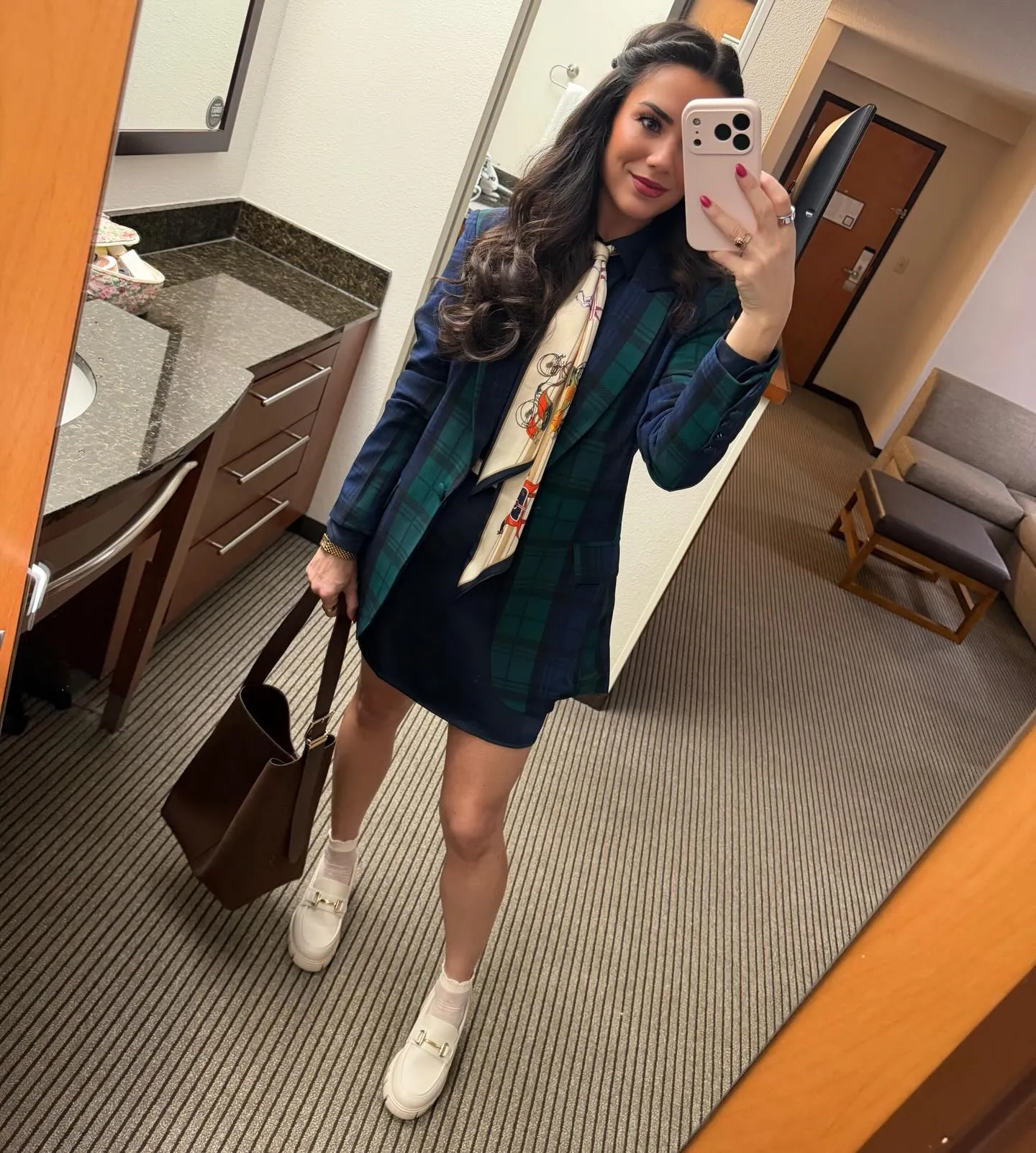 Susanne in a navy and green plaid blazer over a navy shirtdress with a cream carriage-print scarf tied like a tie, brown tote and cream lug-sole loafers