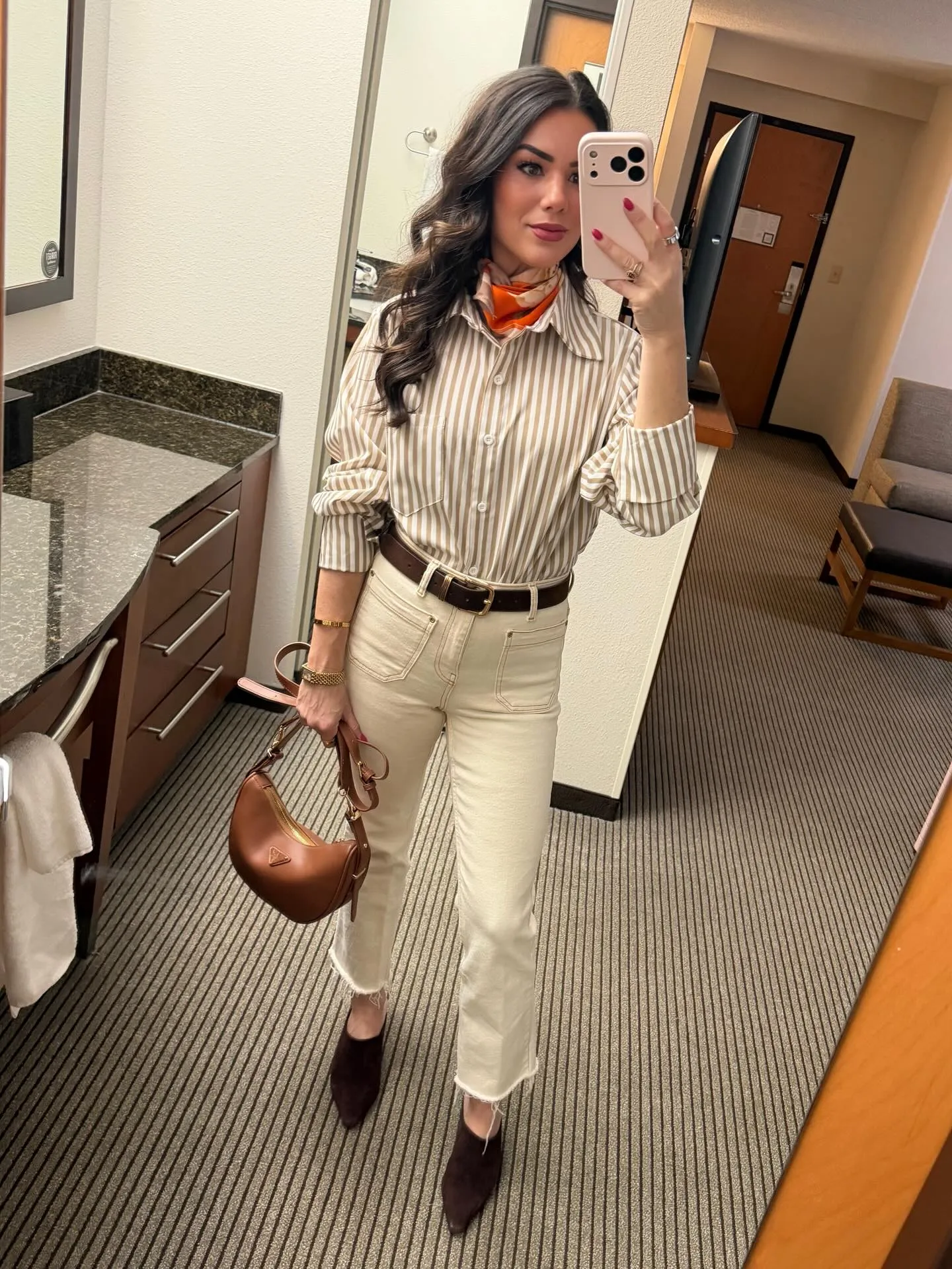 Susanne in a tan striped button-down and cream frayed-hem jeans with a brown belt, orange scarf at her neck, brown shoulder bag and chocolate suede mules