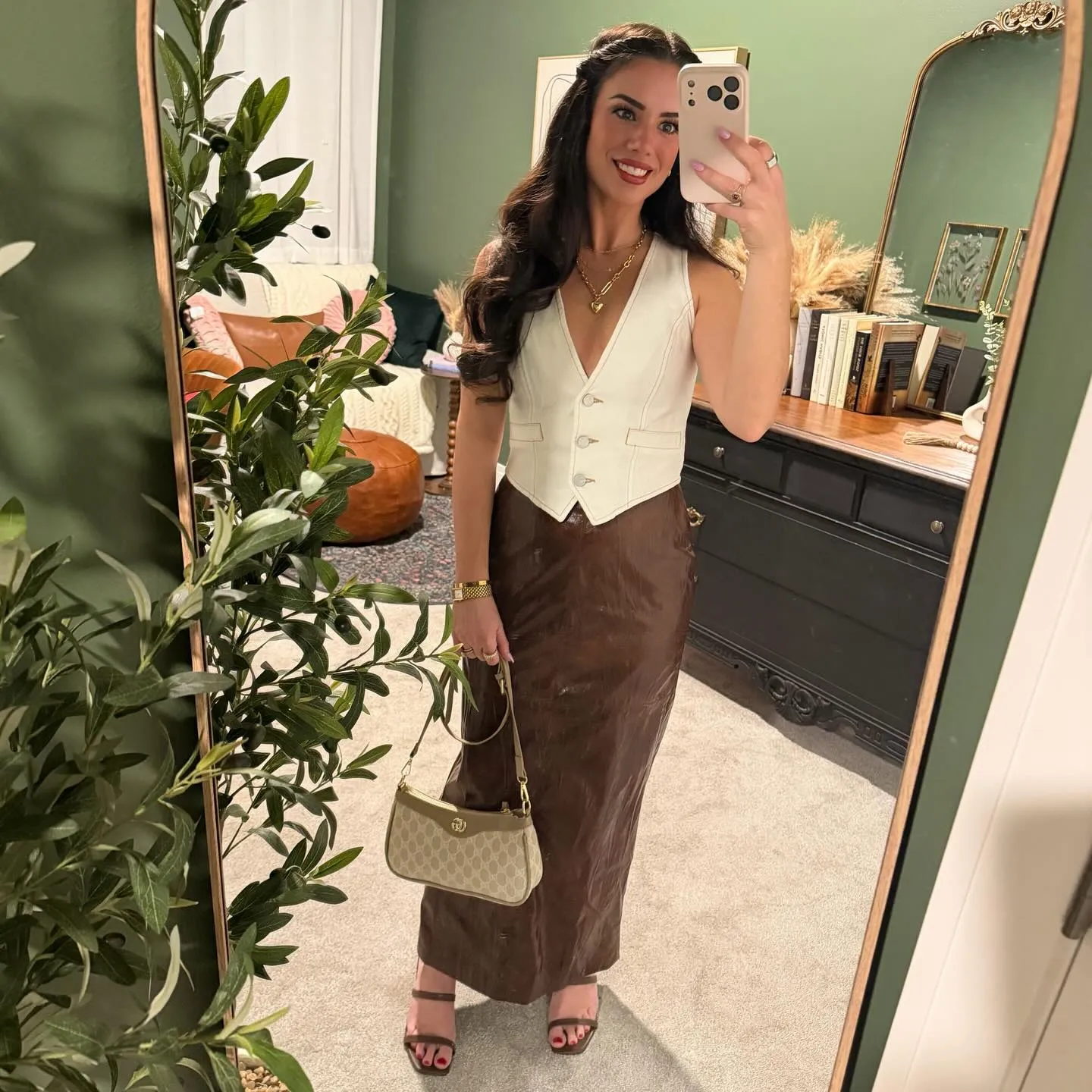 Susanne in a cream denim vest top and chocolate brown leather maxi skirt with layered gold necklaces, monogram bag and brown strappy heels