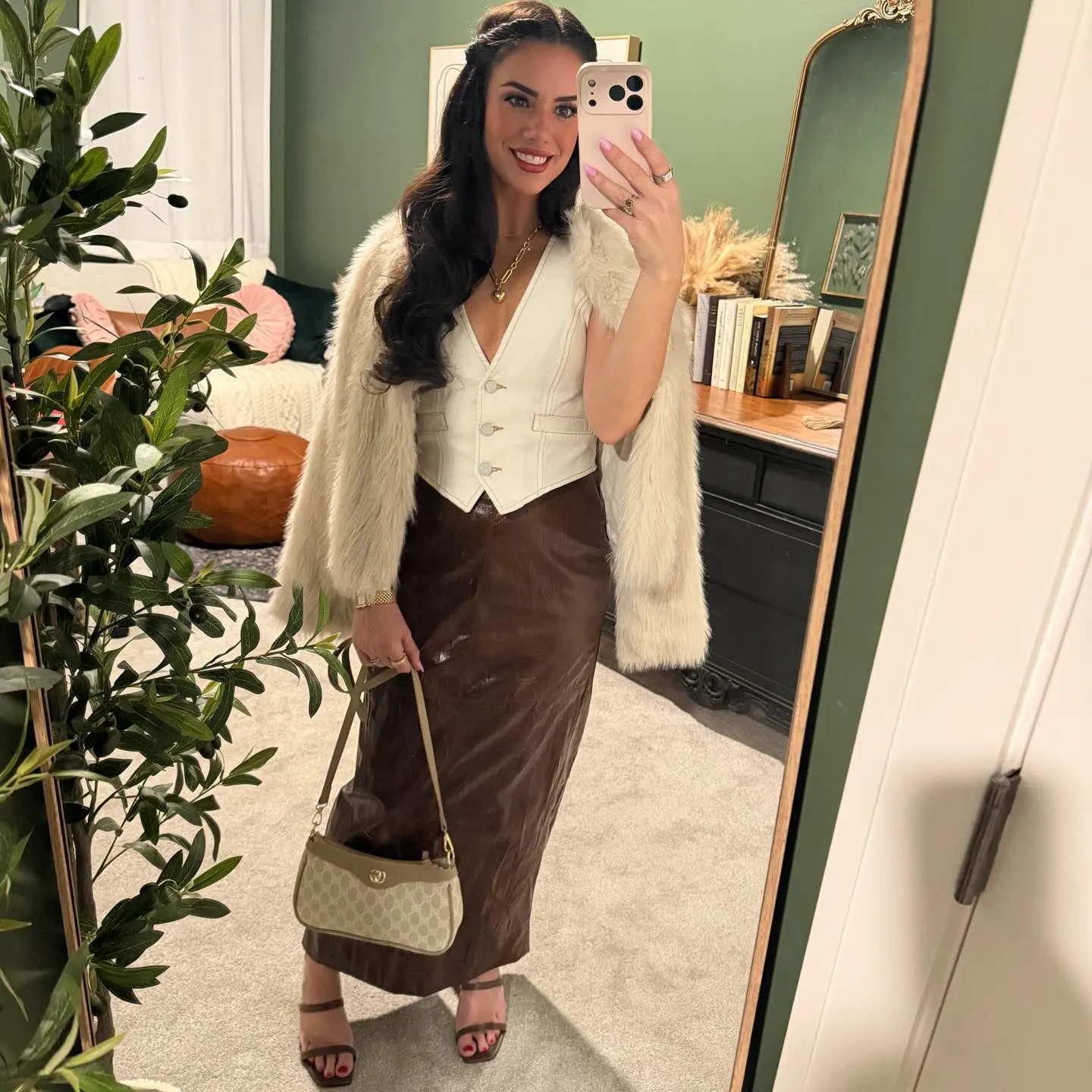 Susanne with a cream fur jacket draped over her shoulders atop the cream vest and brown leather maxi skirt, monogram shoulder bag in hand