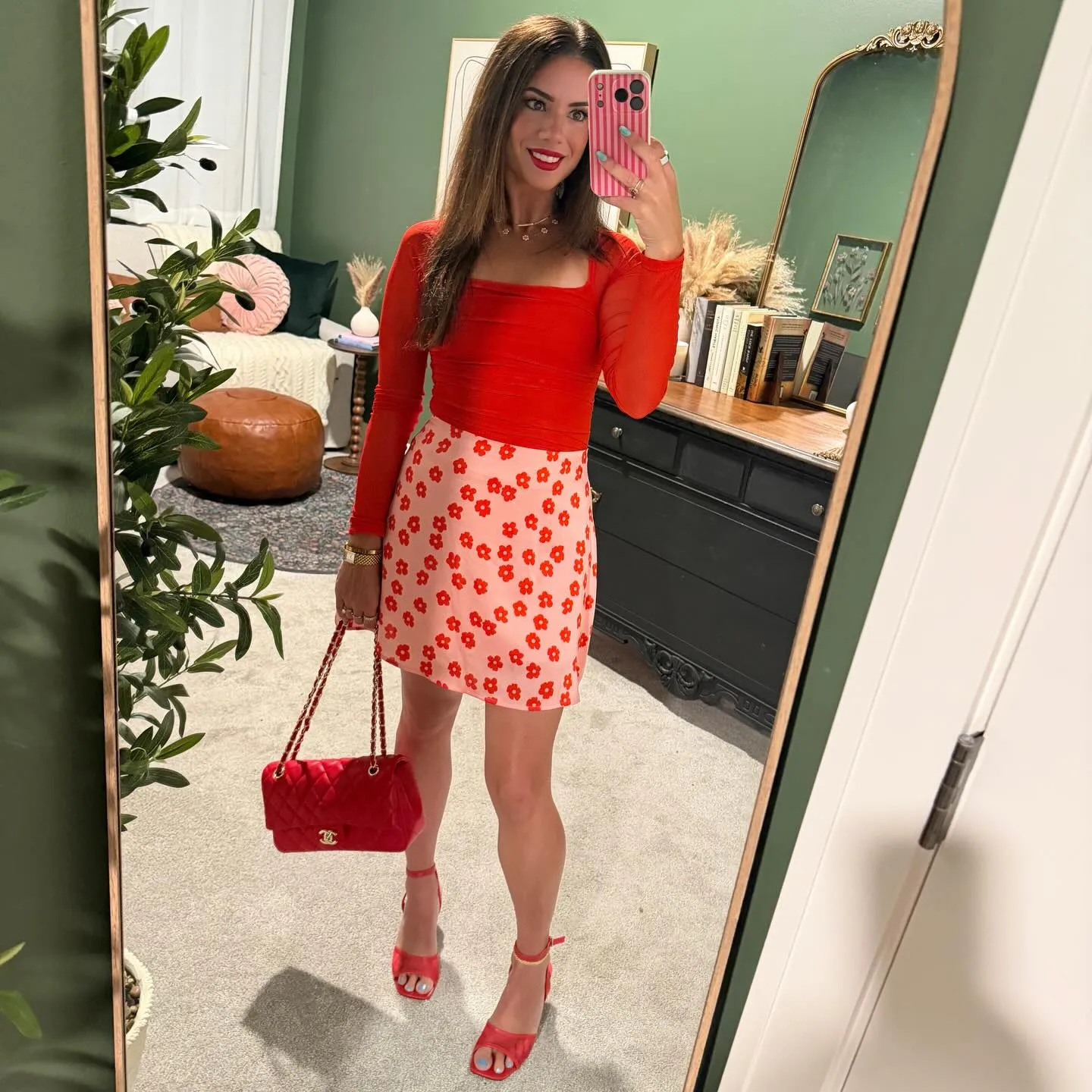 Susanne in a red long-sleeve top and light pink skirt printed with red flowers, red quilted bag, red ankle-strap heels and a red lip