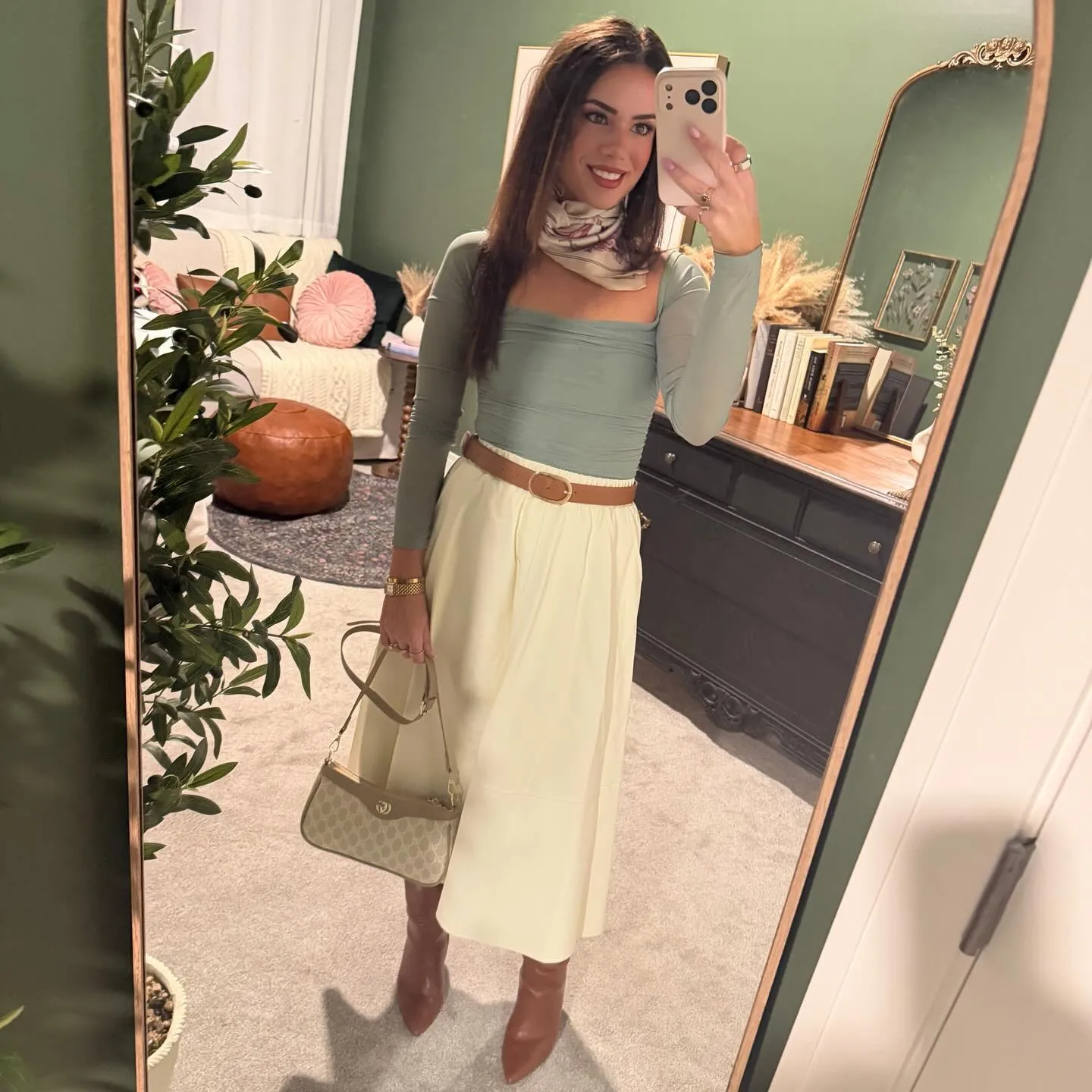 Susanne in a sage green mesh top and cream belted midi skirt with a silk scarf at her neck, monogram shoulder bag and cognac knee-high boots