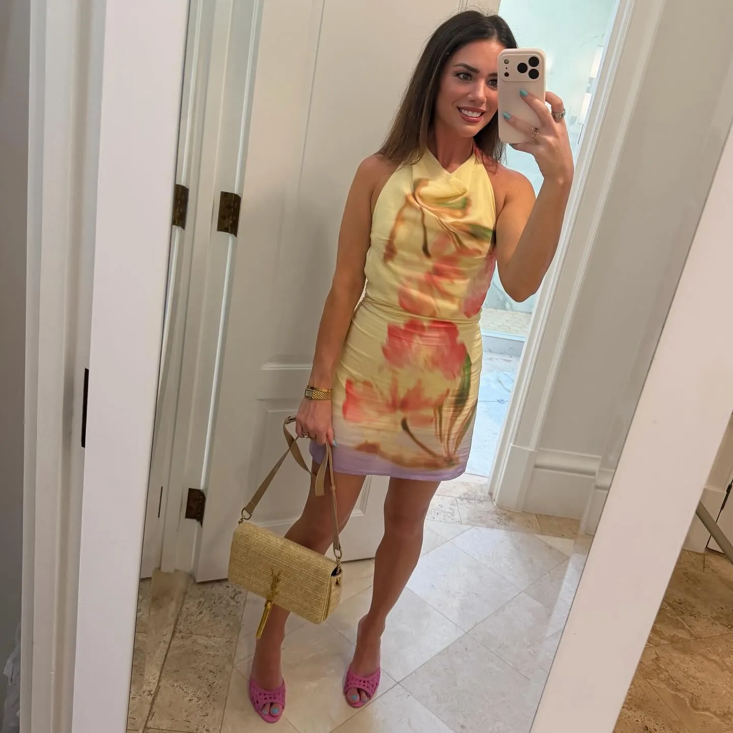 Susanne in a pale yellow halter mini dress with an oversized pink floral print, straw tassel shoulder bag and pink woven mules