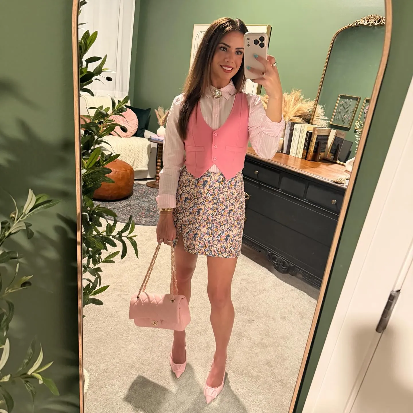 Susanne in a pink vest over a pink striped button-down with a jeweled brooch at the collar, floral mini skirt, pale pink quilted bag and pointed pink heels
