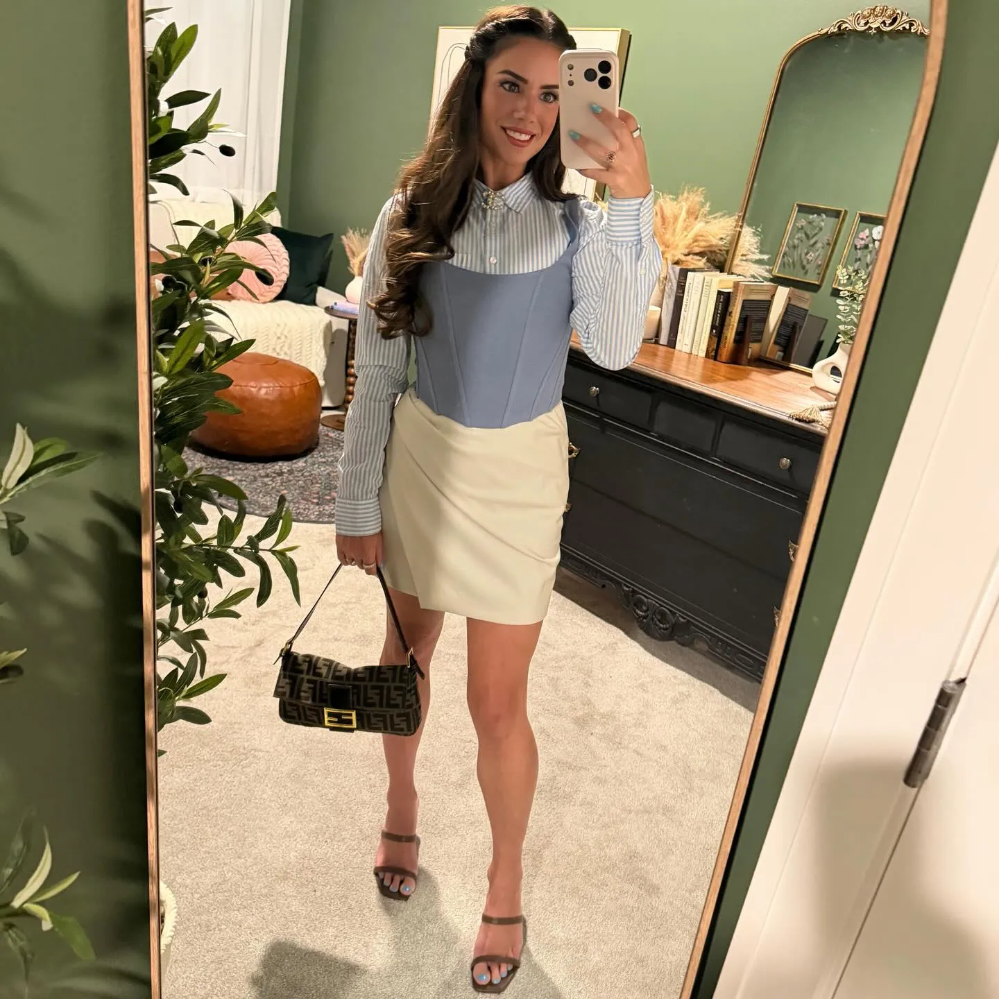 Susanne in a light blue corset layered over a blue striped button-down with a cream leather skirt, brown baguette bag and brown strappy heels