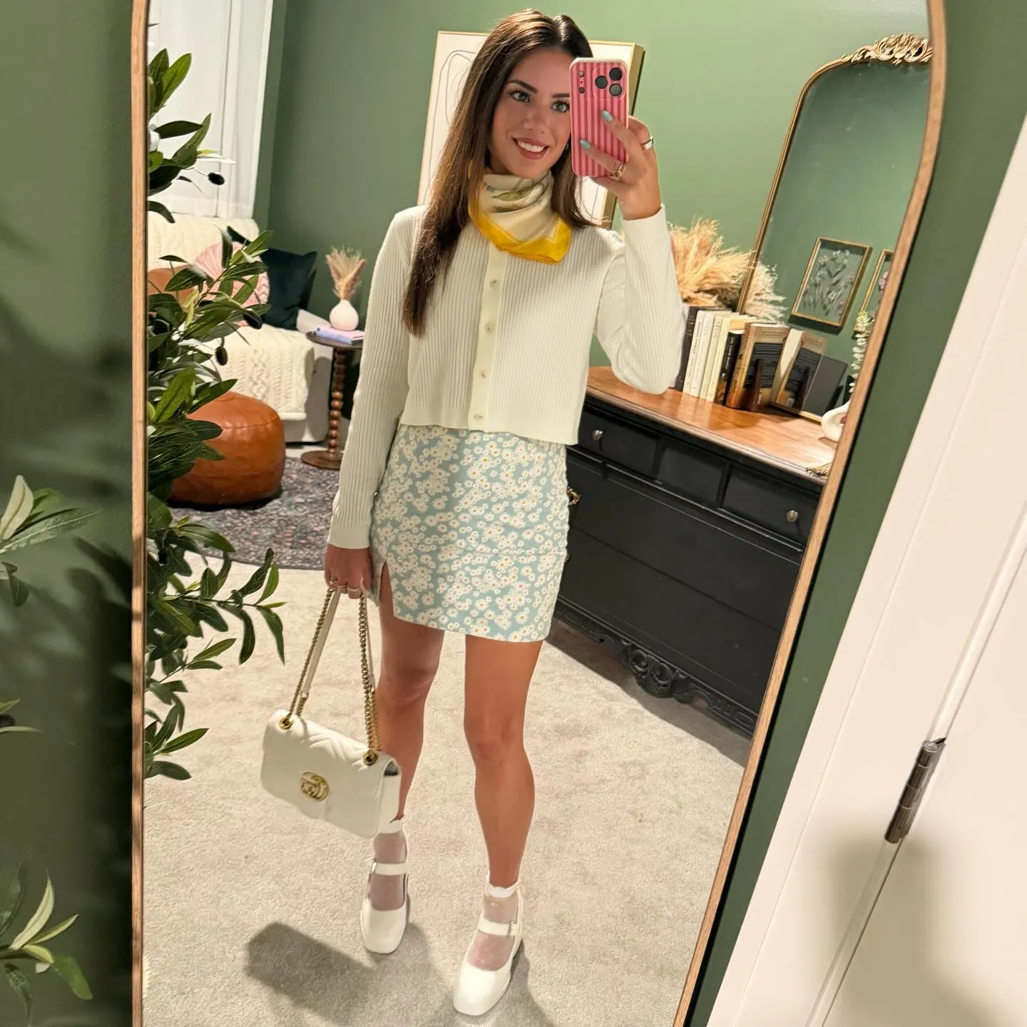 Susanne in a cream cropped sweater and light blue daisy-print mini skirt, yellow-trimmed scarf at her neck, white Mary Janes with sheer ruffled socks