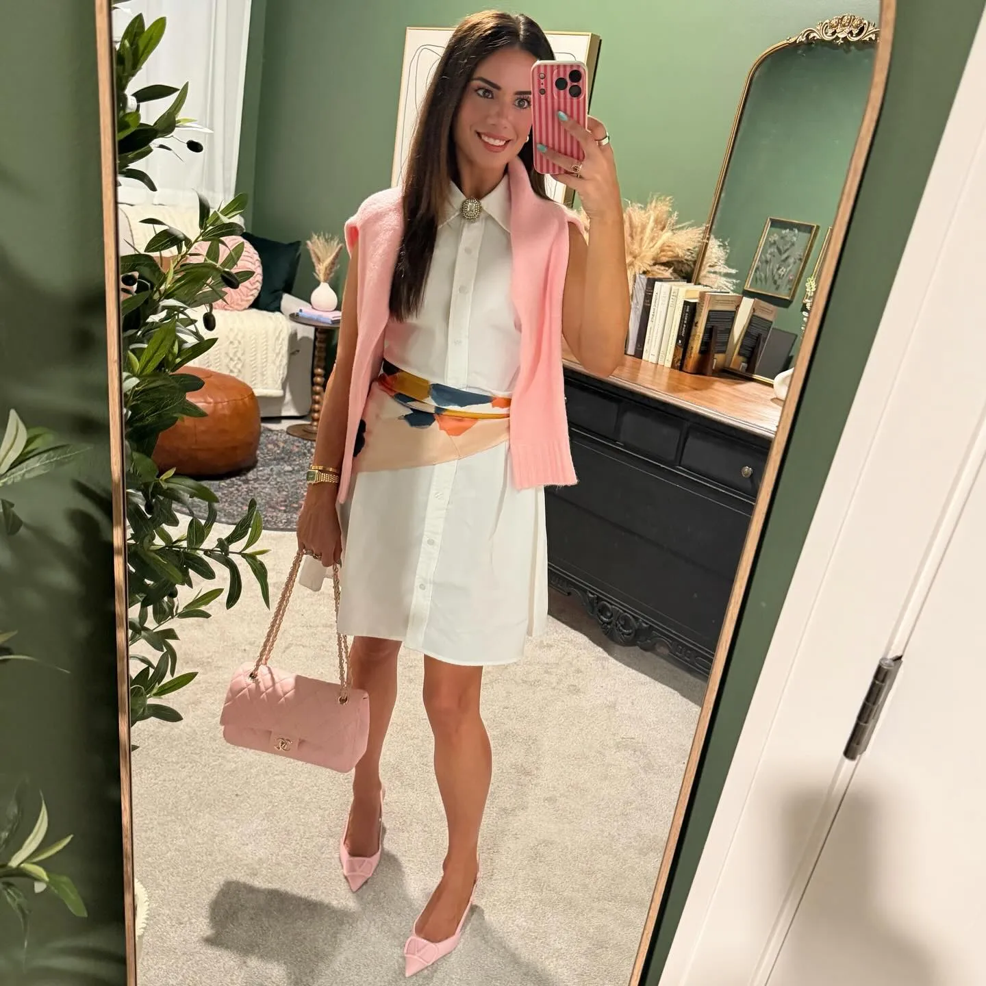 Susanne in a white collared shirtdress with a pink scarf tied at the waist, pink sweater draped over her shoulders, pink pointed heels and quilted pink bag