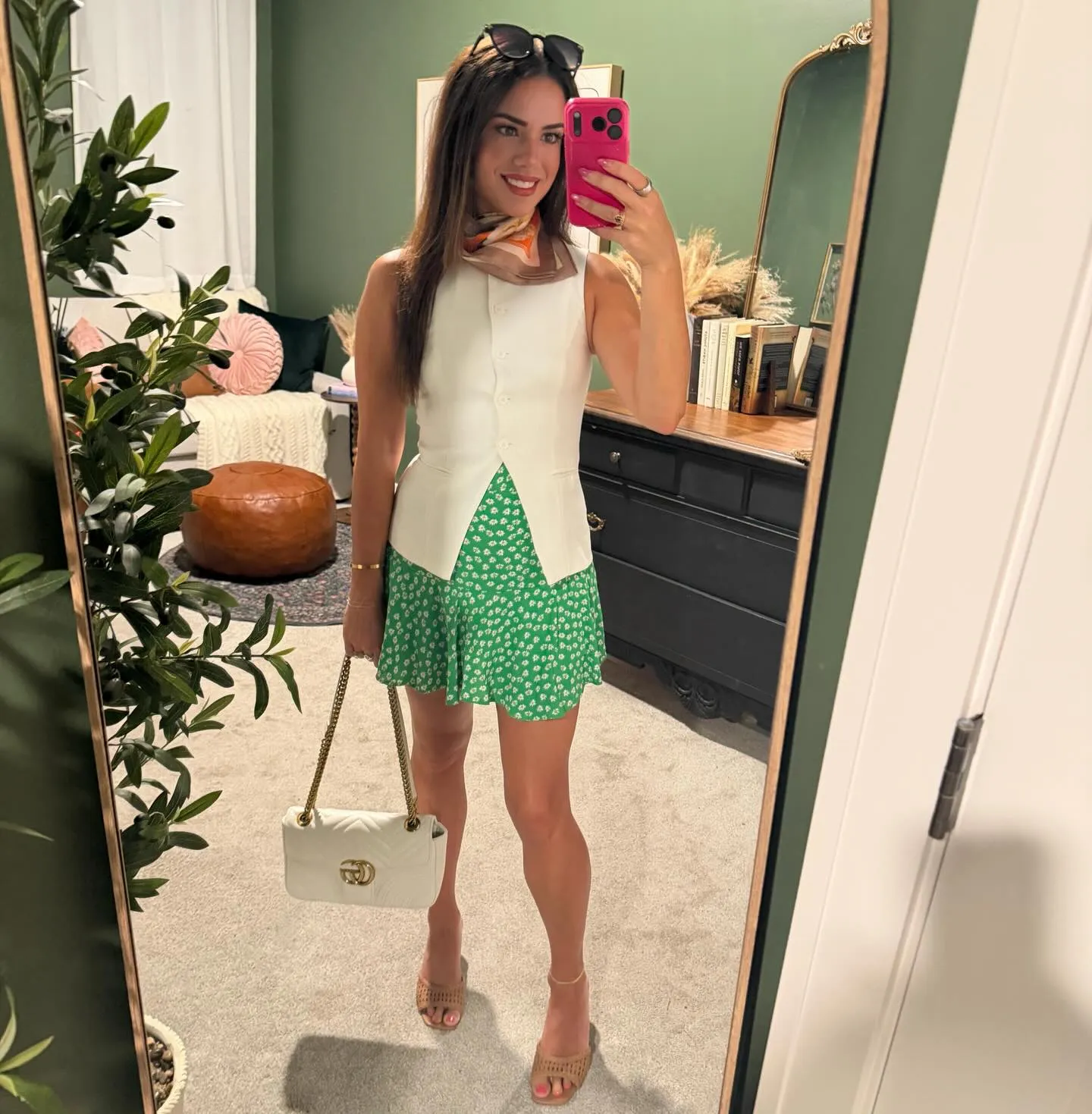 Susanne in a white sleeveless vest and green daisy-print flounce skirt with a silk scarf at her neck, white chain-strap bag and tan mules