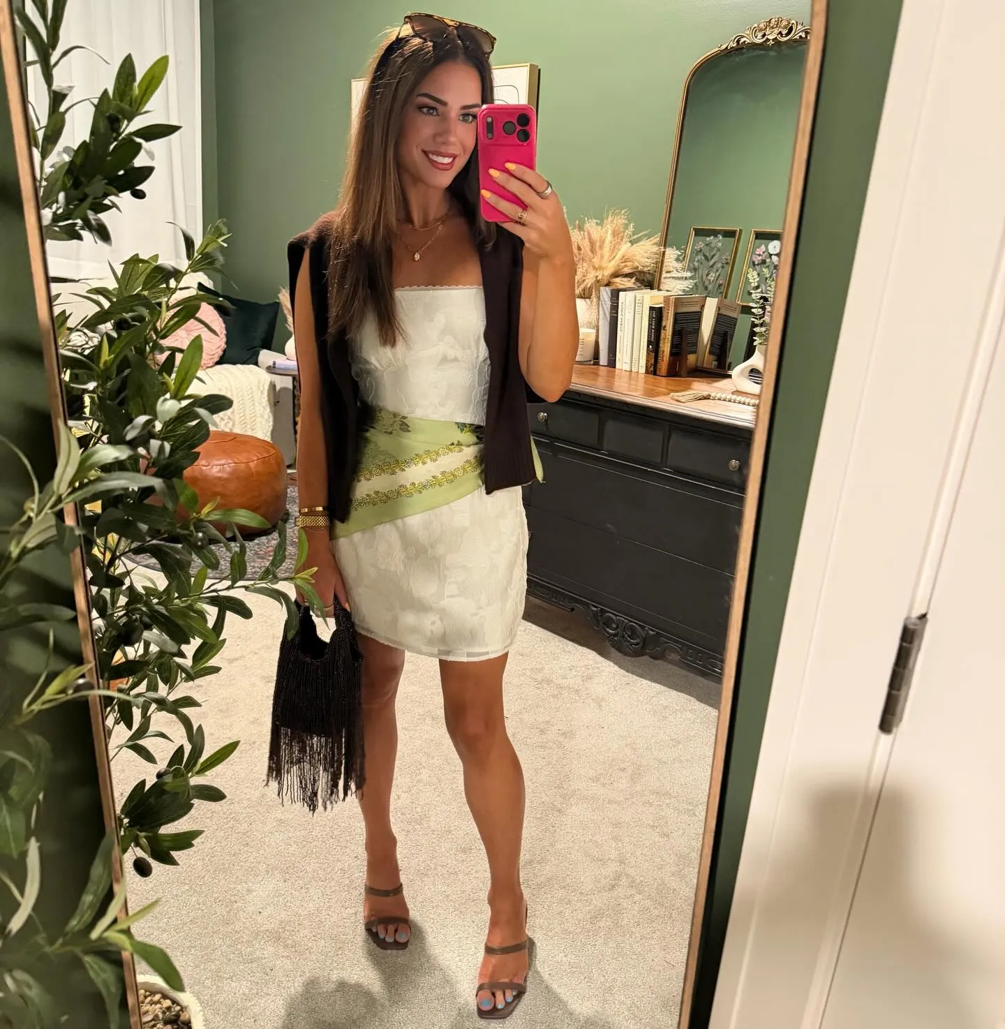 White floral embossed strapless mini dress with a lime green floral scarf at the waist, brown sweater over the shoulders, brown heeled sandals and a black fringed beaded bag.