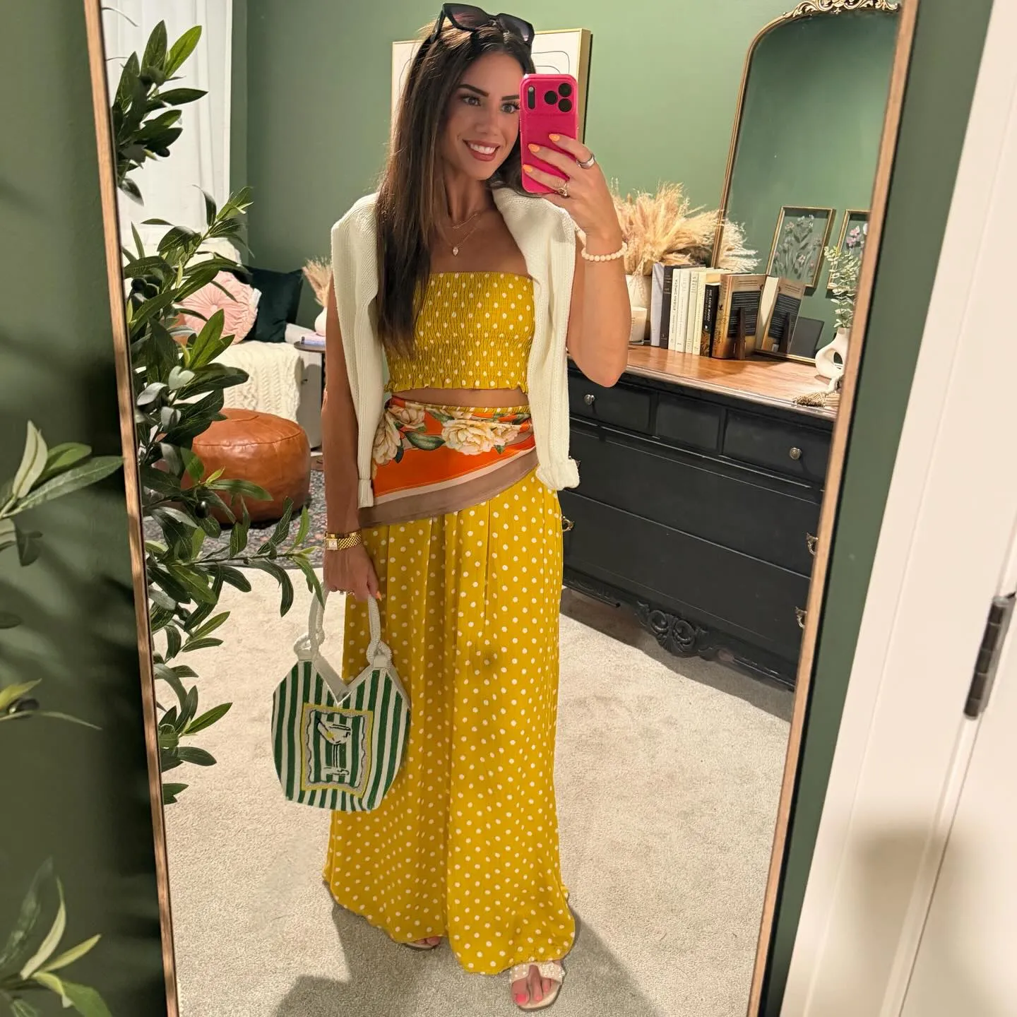 Susanne in a mustard polka dot tube top and maxi skirt set with an orange floral scarf tied at the waist, a white sweater over her shoulders, holding a green striped beaded bag, mirror selfie in her green dressing room
