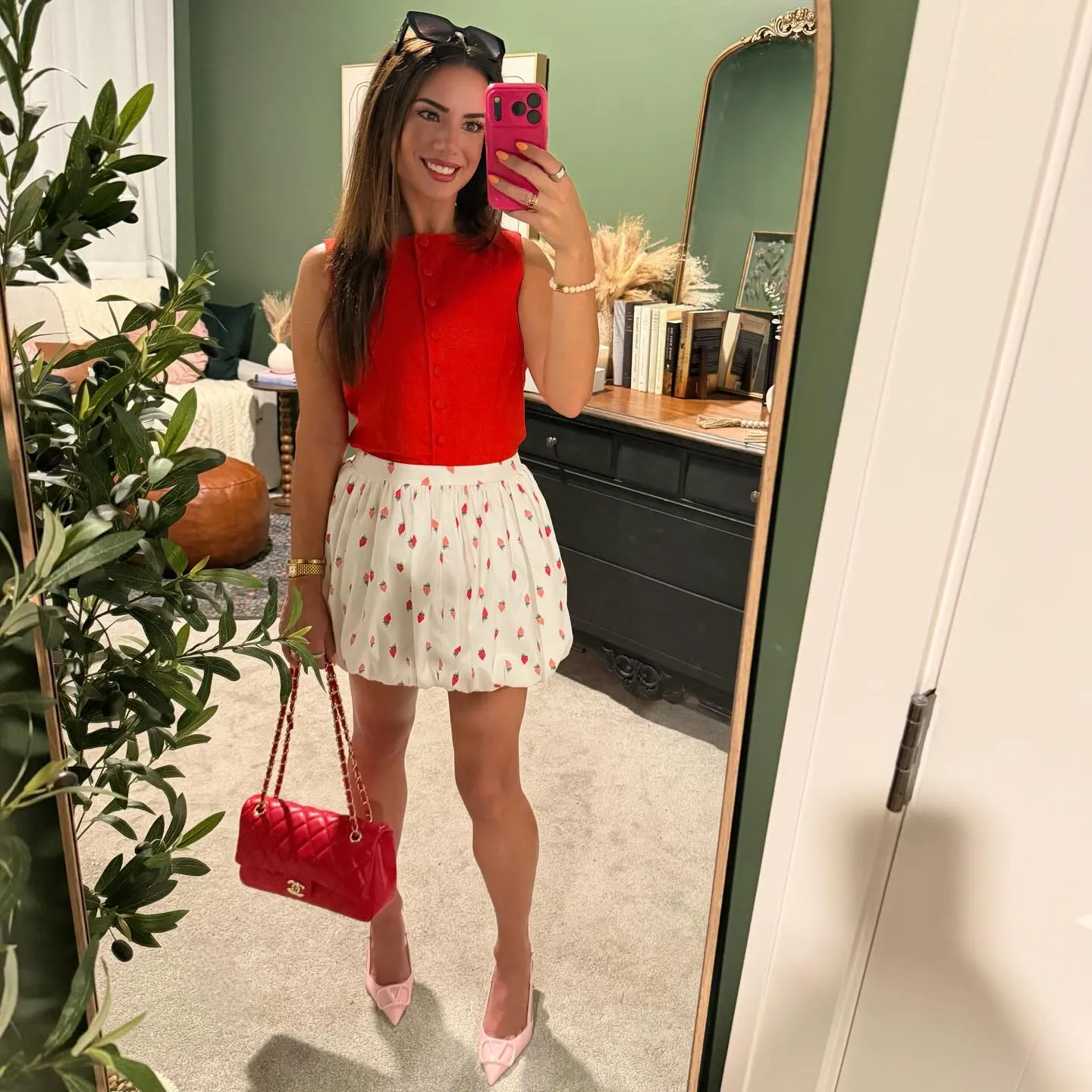 Mirror selfie in a red button-front linen vest tucked into a cream bubble-hem mini skirt with strawberry print, red quilted bag and pink pointed heels.