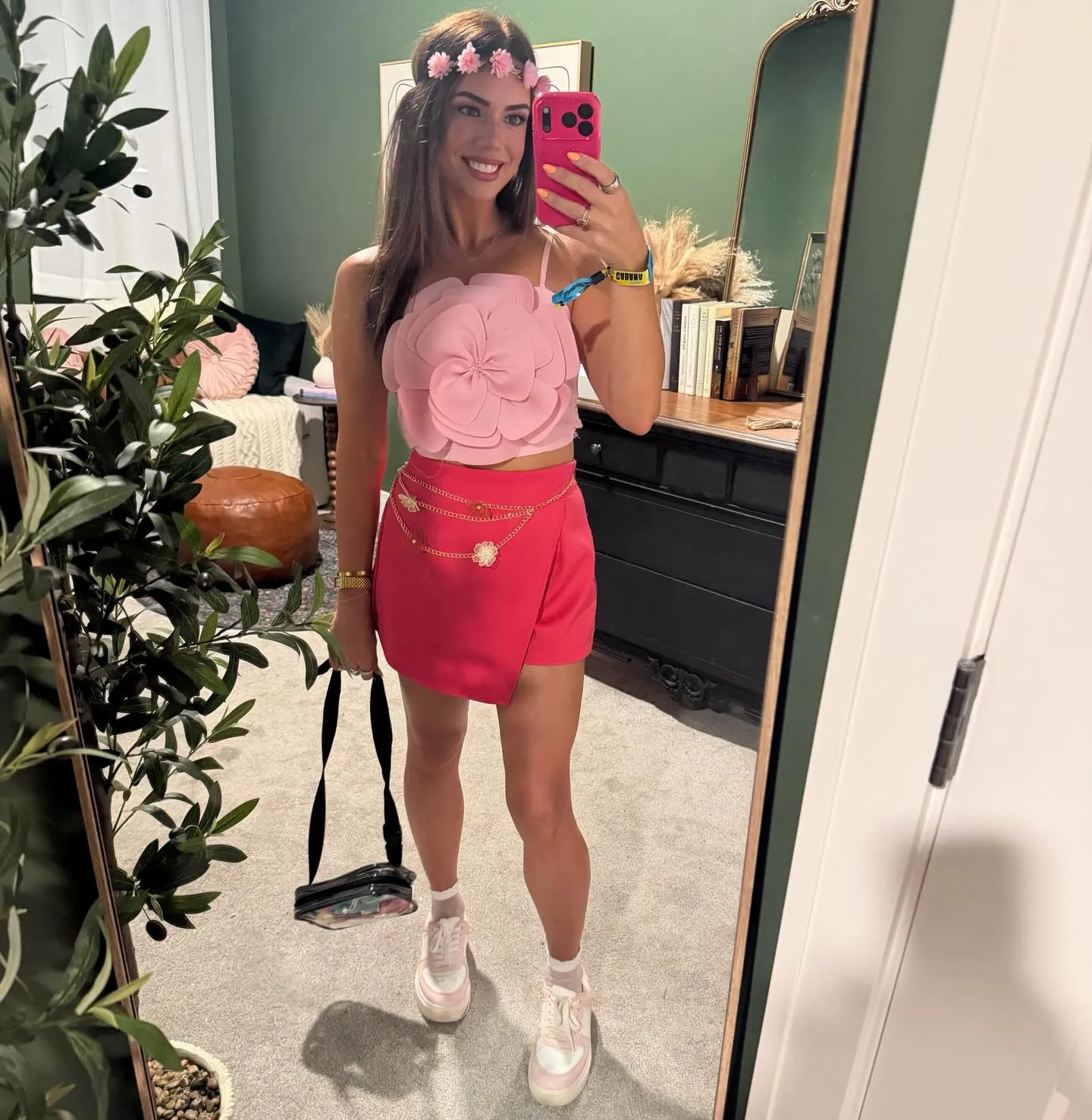 Mirror selfie in a light pink crop top with an oversized 3D flower, hot pink asymmetric mini skirt, gold chain belt, pink sneakers and a flower crown.