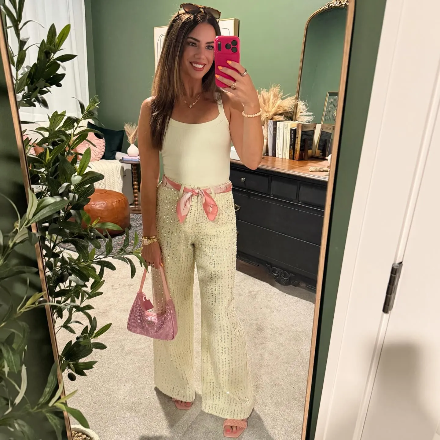 Mirror selfie in a cream tank and sequined cream wide-leg jeans with a pink floral scarf tied at the waist, pink bag and sandals.