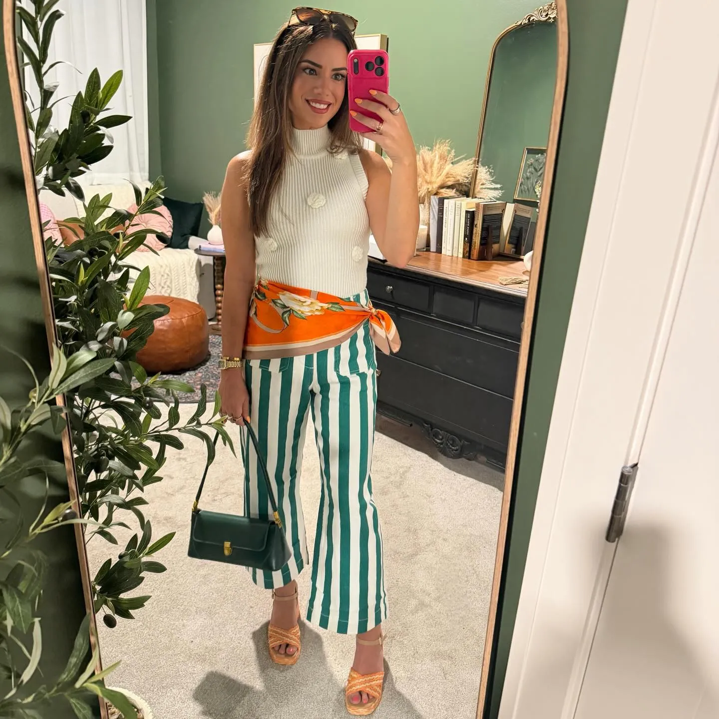 Cream sleeveless mock neck knit top with 3D flowers, green and white striped cropped wide-leg pants, an orange floral waist scarf, green shoulder bag and orange raffia heels.