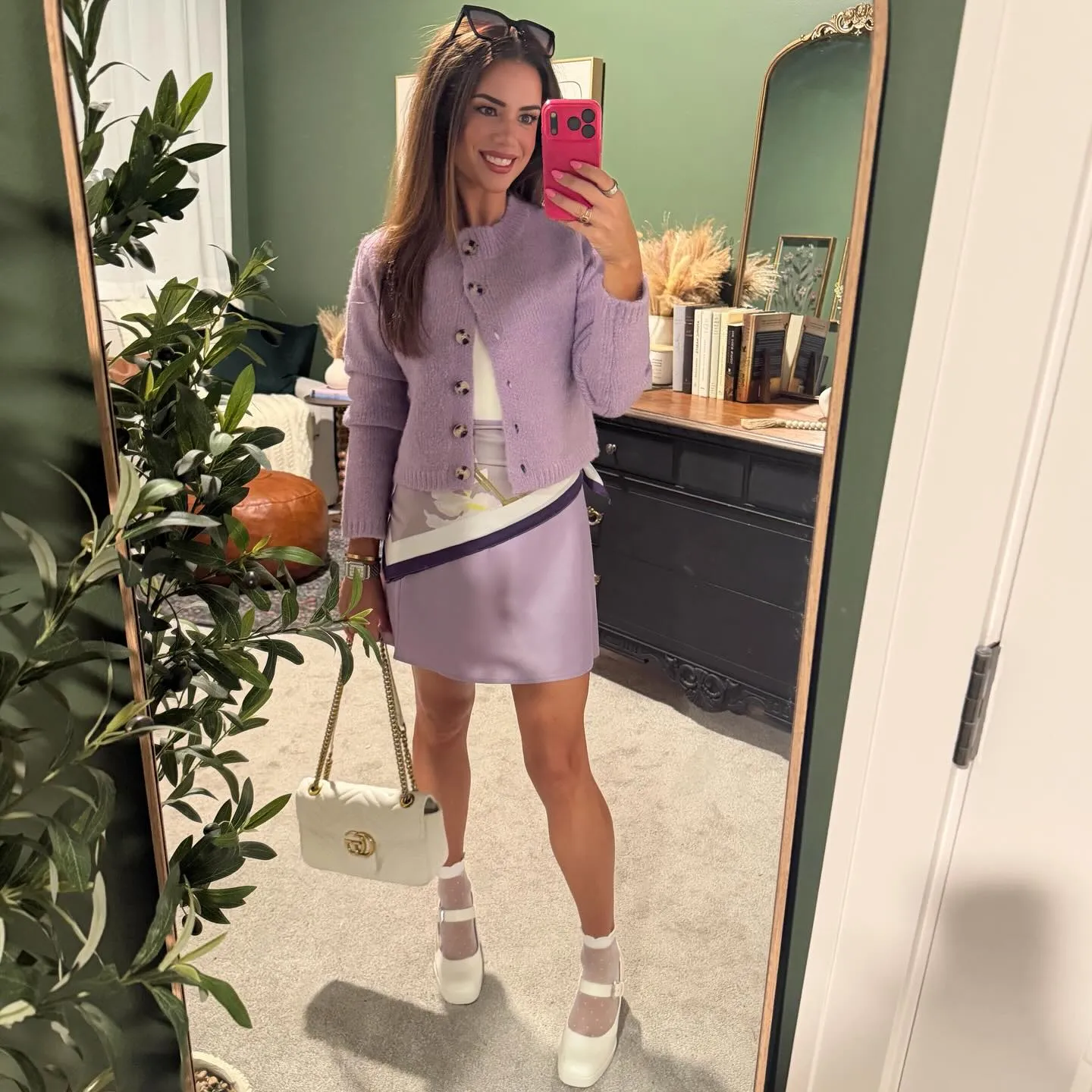 Lavender chunky cardigan with a matching satin mini skirt, floral scarf at the waist, sheer polka dot socks, white platform Mary Janes and a white chain bag.